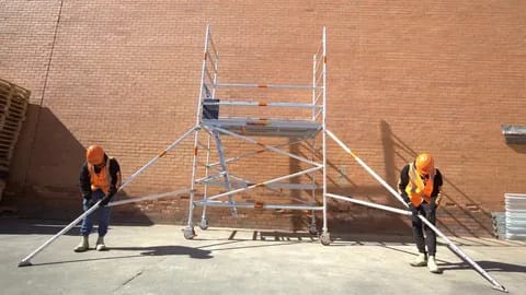 Workers stabilizing a mobile scaffolding tower against a brick wall.