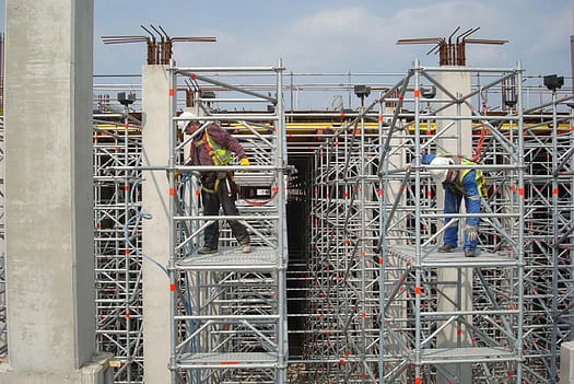 Construction workers assembling heavy-duty scaffolding between concrete columns
