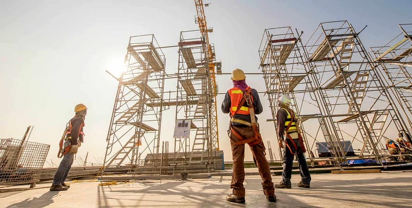 Construction workers observing tall scaffold structures at a building site.